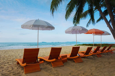Deck chairs and parasols on beach against sky