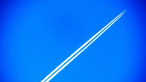 Low angle view of vapor trails against clear blue sky