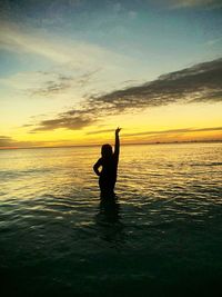 Silhouette woman posing in sea against sky during sunset