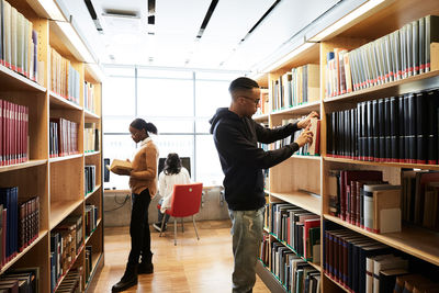 Students searching book while woman using computer in library at university