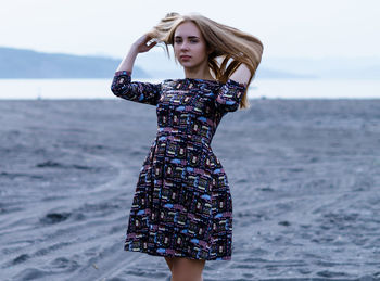 Portrait of young woman standing at beach against sky