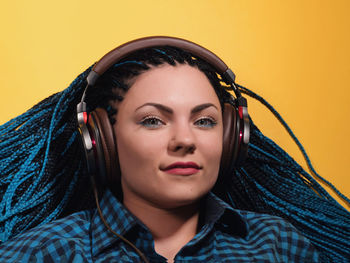 Portrait of young woman listening to music on headphones against yellow background