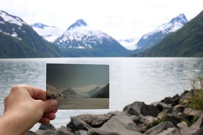 Hand holding rock by lake against mountains