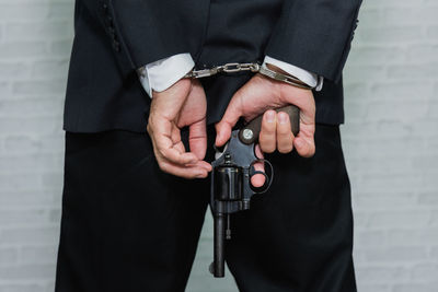 Midsection rear view of businessman with handcuffs holding gun