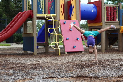 Girl practicing handstand against jungle gym at playground