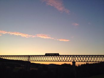 Low angle view of train on silhouette bridge against sky during sunset