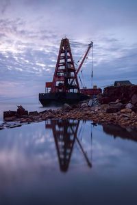 Reflection of metal structure in sea against sky