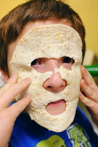 Portrait of boy covering face with flatbread mask
