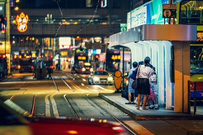 People waiting for tram on street in city at night