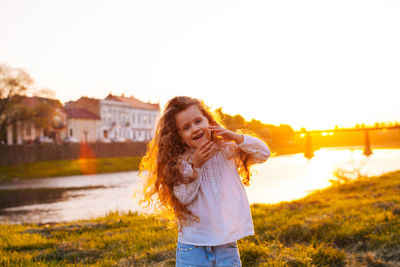 Happy young woman standing on land against sky during sunset