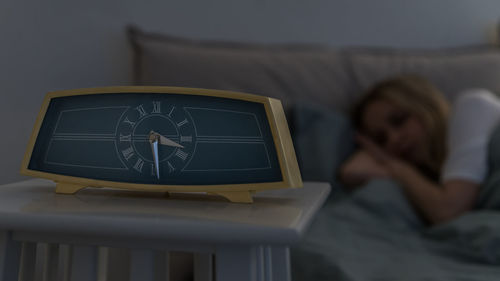 Close-up of clock on table with woman sleeping in background