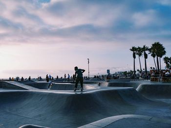 People at skateboarding park against sky during sunset