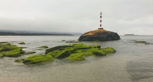 Lighthouse on rocks by sea against sky