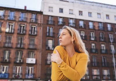 Young woman looking away against buildings in city
