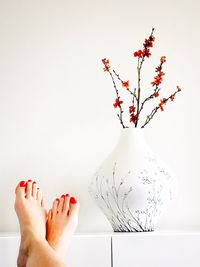 Low section of legs crossed at ankle with vase against wall