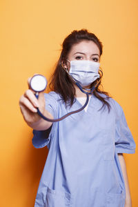 Doctor holding stethoscope against yellow background