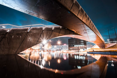 Illuminated bridge over river in city against sky at night