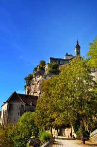 Low angle view of trees and building against blue sky