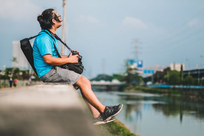 Man using mobile phone while sitting on lake against sky