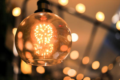 Close-up of illuminated light bulb hanging against wall