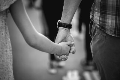 Midsection of man holding hands with daughter while walking on road