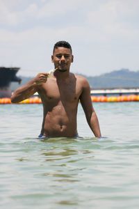 Shirtless man eating ice cream while standing in sea