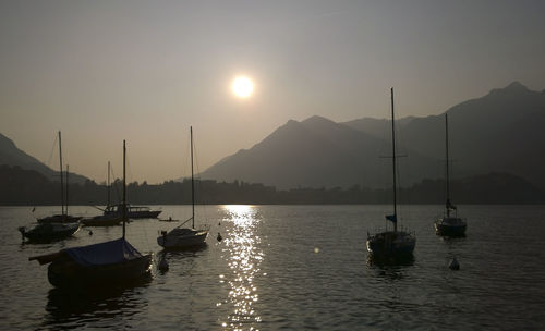 Sailboats moored on sea against sky during sunset