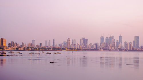 Sea by buildings against sky during sunset