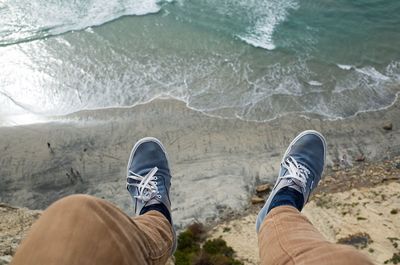 Low section of man sitting on cliff at beach