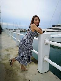 Portrait of smiling woman standing by railing at harbor