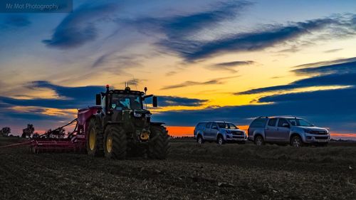 Tractor on field against sky during sunset