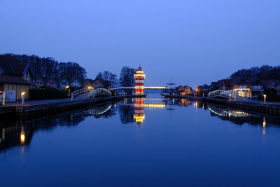 Illuminated buildings by river against sky at night