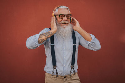 An older man in hipster clothes and glasses and long white beard listens to music