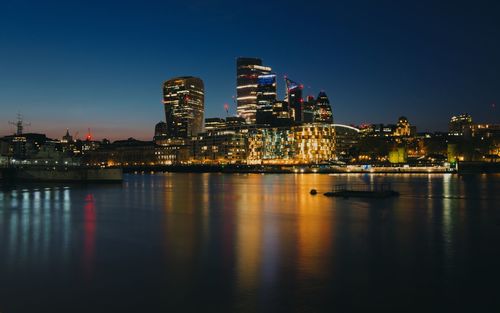 Illuminated buildings by river against sky at night