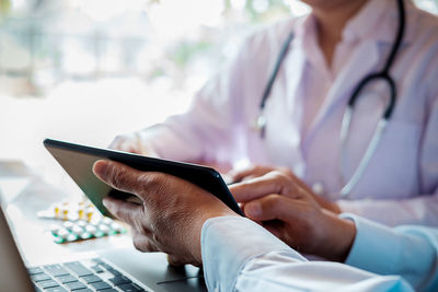 Midsection of doctors discussing over digital tablet