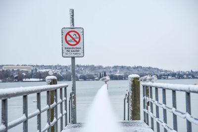 Close-up of sign by railing against river during winter