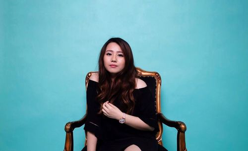 Portrait of a young woman sitting against blue background