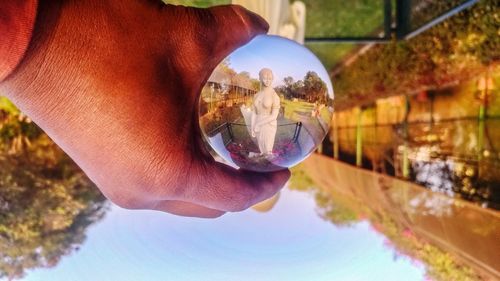 Close-up of hand holding crystal ball reflection in water