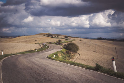 Road passing through field against cloudy sky