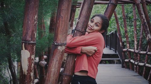 Portrait of smiling young woman standing by tree trunk