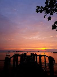 Silhouette wooden posts on beach against sky during sunset