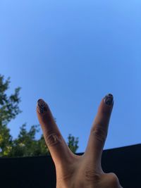 Cropped hand of woman gesturing peace sign against clear blue sky