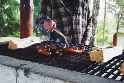 Midsection of man grilling sausages on barbecue at forest