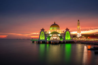 Illuminated melaka straits mosque by sea against sky during sunset