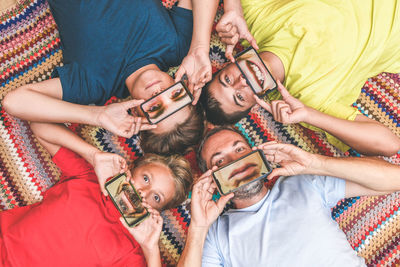 Directly above shot of siblings with father holding smart phone over face while lying on rug