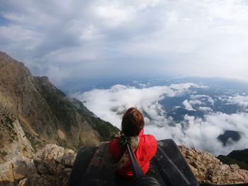 Rear view of woman relaxing on mountain peak against cloudy sky