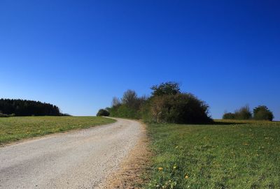 View of empty road on field against clear blue sky