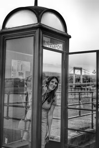 Portrait of smiling mature woman standing in telephone booth