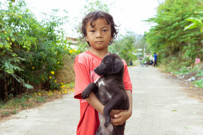 A girl in rural thailand, holding a dog along the road, teasing each other, dog, cute