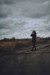 Side view of man photographing on field against sky